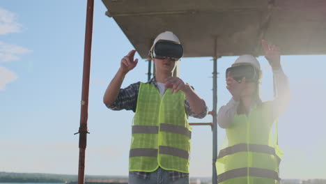 A-man-and-a-woman-engineers-at-a-construction-site-in-VR-glasses-manage-the-construction-of-a-building-discussing-a-development-plan